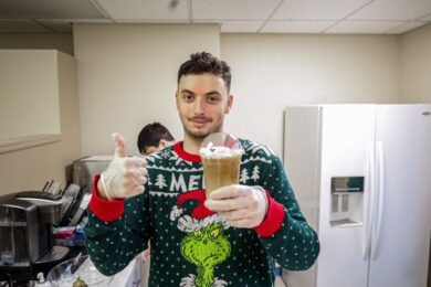 A student working at Brookville Beans gives a thumbs up while holding an iced coffee drink that he made.